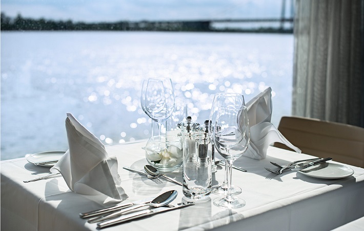A table next to a window with a shimmering river view on-board Emerald Liberte